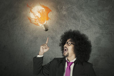 Digital composite image of businessman pointing at burning light bulb against wall
