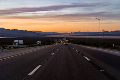 Road by mountains against sky during sunset