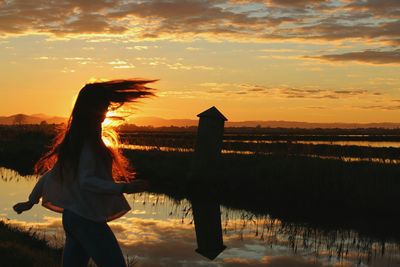 Woman standing by lake against sky during sunset