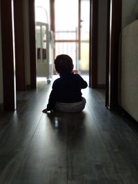 Rear view of girl sitting on floor at home