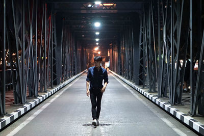Full length rear view of man walking on illuminated bridge at night