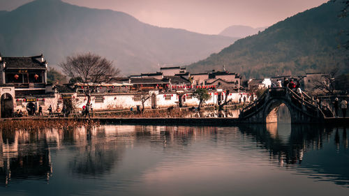 Bridge over river by buildings against sky at dusk