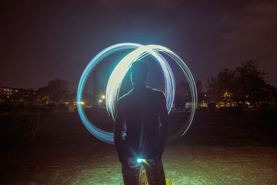 Rear view of silhouette man standing by illuminated light against sky at night