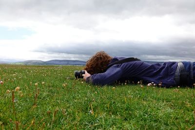 Man sitting on grassy field against cloudy sky