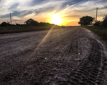 Road by agricultural field against sky during sunset