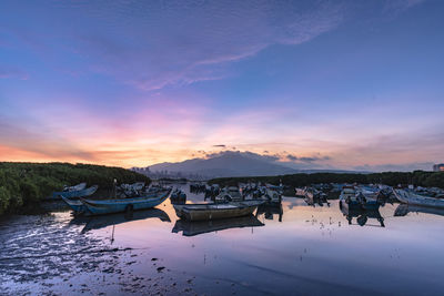 Boats moored in lake against sky during sunset