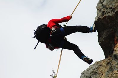 Low angle view of man climbing on rock against sky