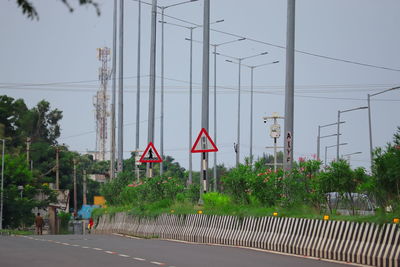 Road sign by trees against sky in city