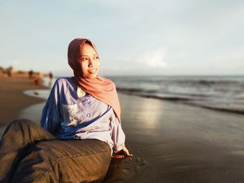 Young woman sitting on shore at beach against sky