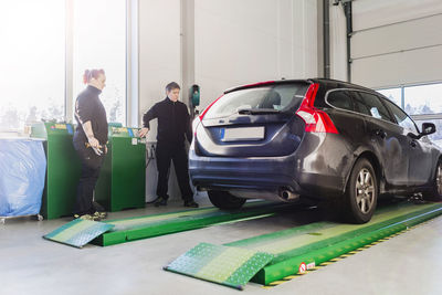 Full length of mechanics looking at car on hydraulic lift at auto repair shop