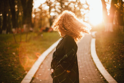 Young red head woman tossing hair while walking in park in autumn