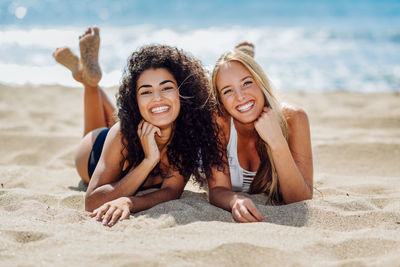 Portrait of smiling young women lying on front at beach