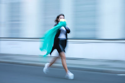 Woman holding scarf running on road in city