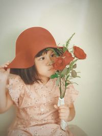 Close-up of girl holding red flowering plant against wall