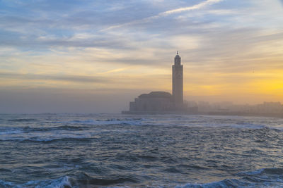 Sea and buildings against sky during sunset