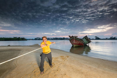 Man pulling old ship from lake against cloudy sky during sunset