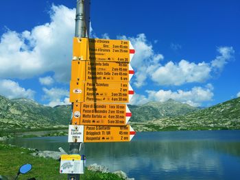 Information sign by lake against sky