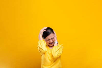 Woman with headache standing against yellow background