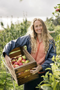 Smiling woman harvesting apples in orchard