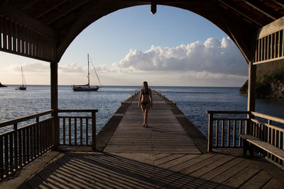 Woman in bikini walking on pier over sea seen from gazebo