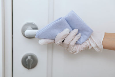 Hands of person wearing glove cleaning handle of door