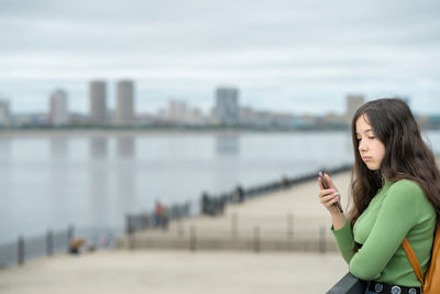 Portrait of young woman standing against river