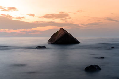 Rocks in sea against sky during sunset