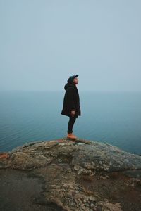 Man standing on rock looking at sea against sky