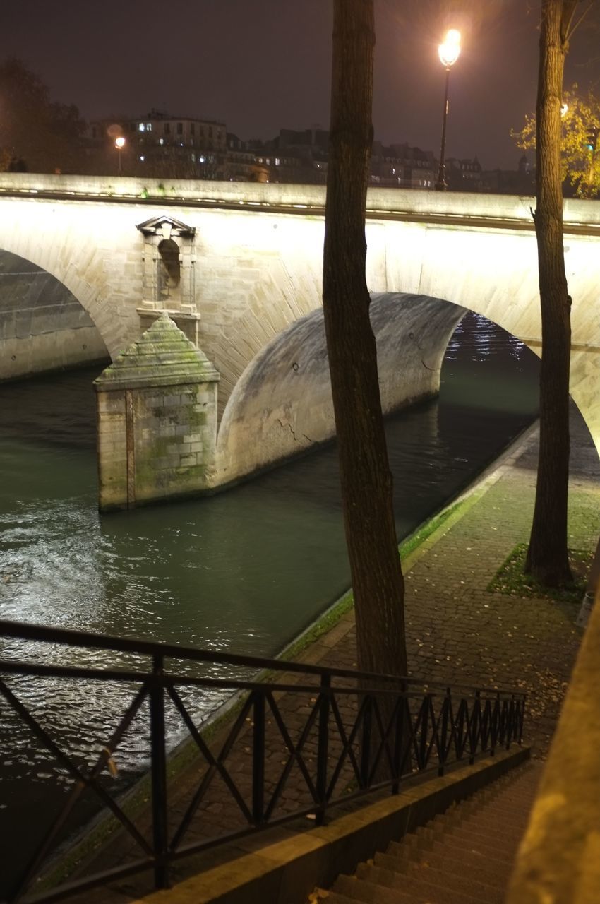 BRIDGE OVER RIVER AGAINST ILLUMINATED LIGHTS AT NIGHT