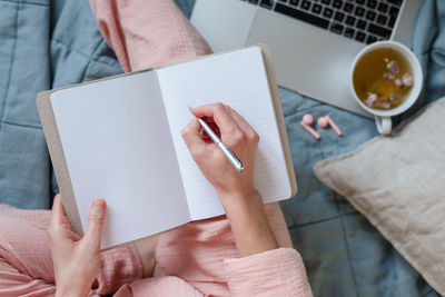 A scene in pastel colors of a woman making notes and drinking hot tea in her bed.