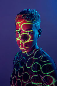 Charming african american female with short hair and in shadow projector light on face looking at camera on purple background in studio