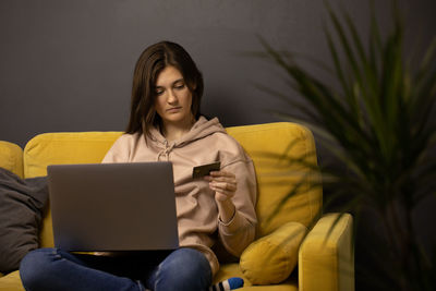 Young woman using mobile phone while sitting on sofa