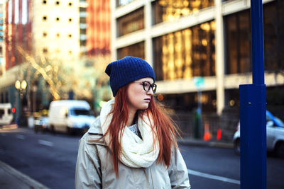 Thoughtful woman wearing knit hat while standing on street in city