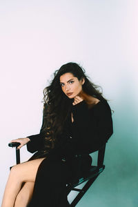 Portrait of beautiful woman sitting on seat against wall