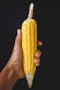 Close-up of hand holding lemon against black background