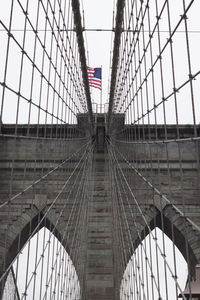 Low angle view of brooklyn bridge with american flag against sky