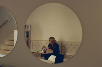 FULL LENGTH PORTRAIT OF WOMAN SITTING ON TABLE IN ILLUMINATED ROOM