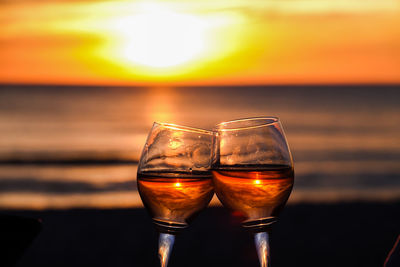 Close-up of beer glass on beach against sky during sunset