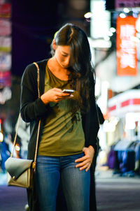 Woman using mobile phone while standing on footpath in taipei city at night
