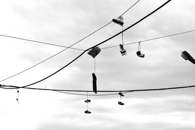 Low angle view of shoes hanging from cables against sky