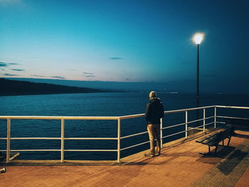 Woman standing on railing against sea at night