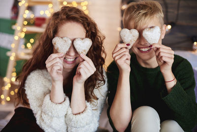 Cheerful sisters holding heart shape cookies at home