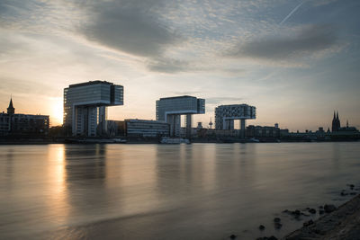 River by city buildings against sky during sunset