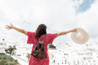 Rear view of woman with arms raised standing against sky