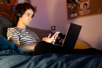 Midsection of man using mobile phone while relaxing on bed at home