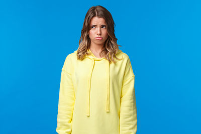 Portrait of young woman standing against blue background