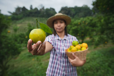 Portrait of woman wearing hat while holding fruits in basket