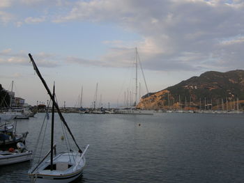 Boats in harbor against cloudy sky