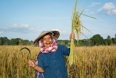 Portrait of smiling senior woman standing in farm against sky