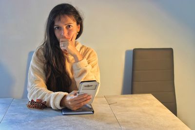 Portrait of young woman using phone while sitting on table